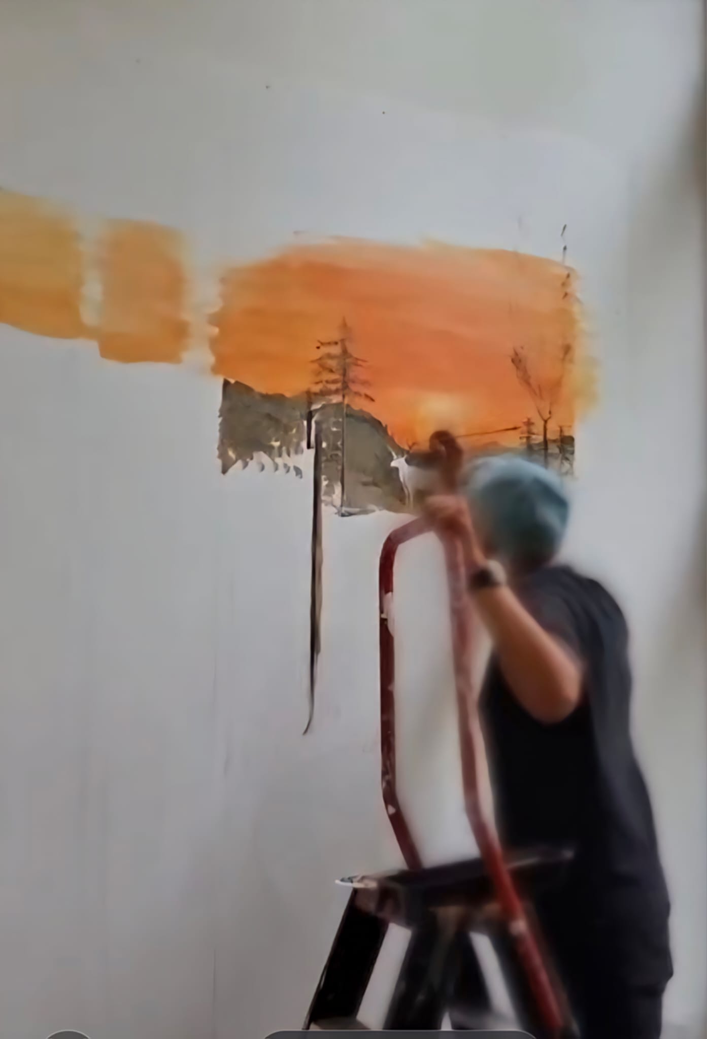 Kunstenaar op een trapje die een zonsondergang op een witte muur schildert